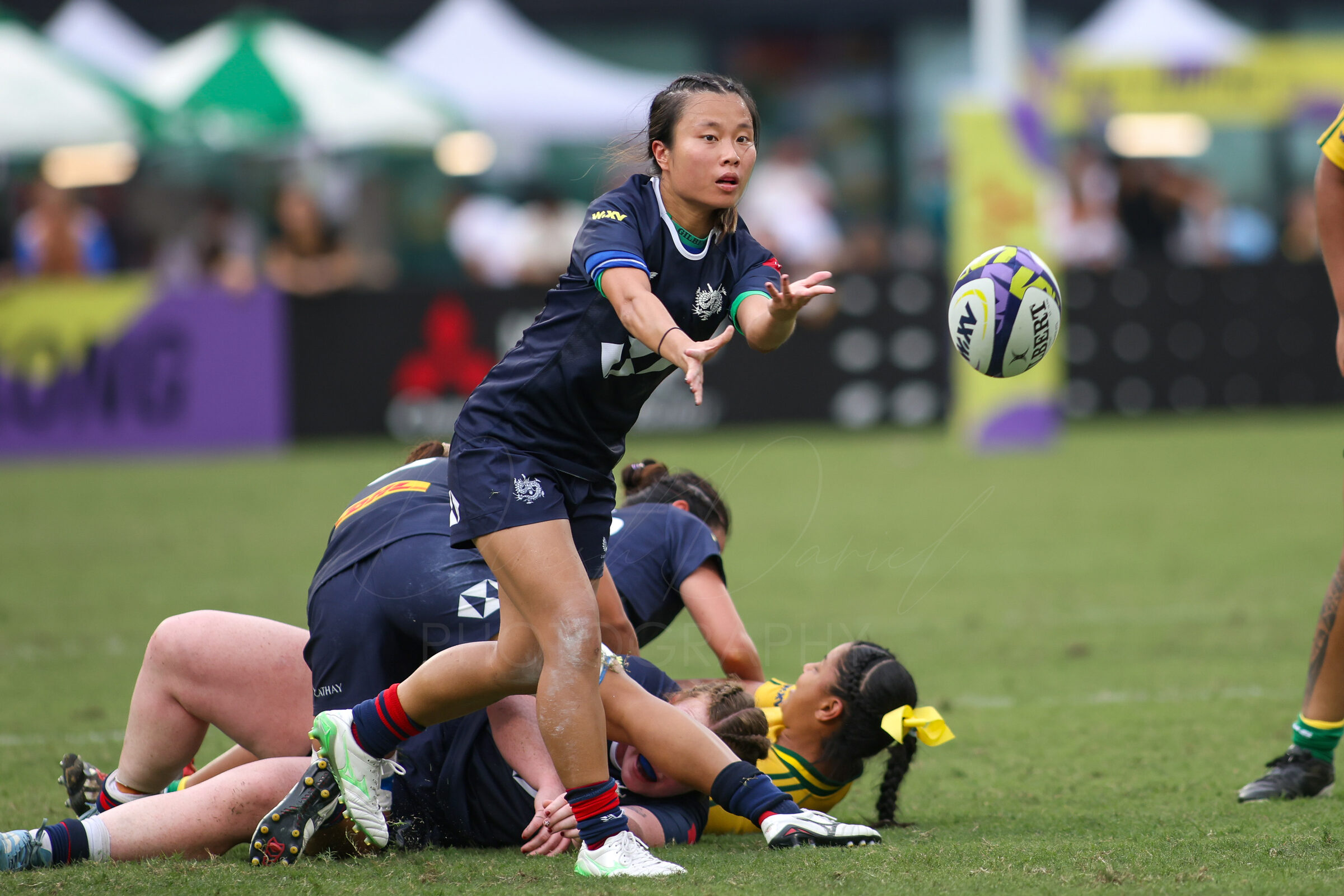 Women’s rugby player releases a pass as teammates ruck below